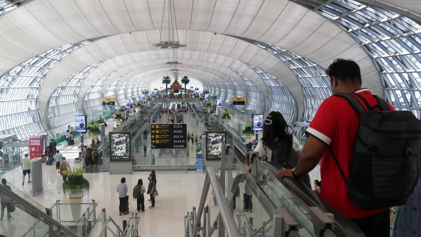 BANGKOK, THAILAND - 16 JULY, 2019: Oriental structure in airport. Traditional Thai construction mounted on glass platforms inside crowded terminal, Suvarnabhumi Airport people whaiting for boarding.
