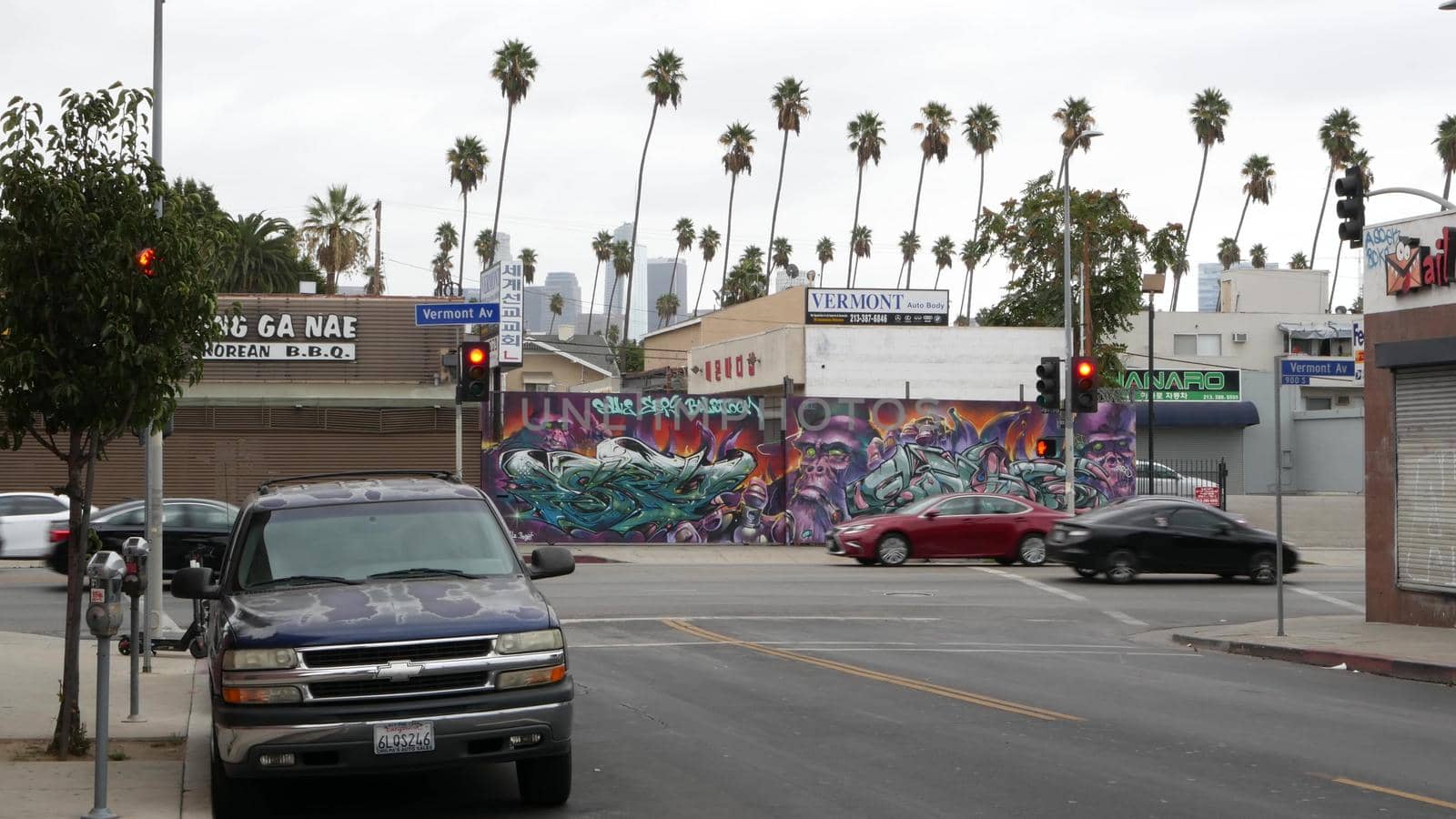 LOS ANGELES, CALIFORNIA, USA - 27 OCT 2019: Urban skyline and palms. LA city aesthetic, graffiti painting on Vermont street. Highrise skyscrapers in downtown of metropolis. Typical road intersection.