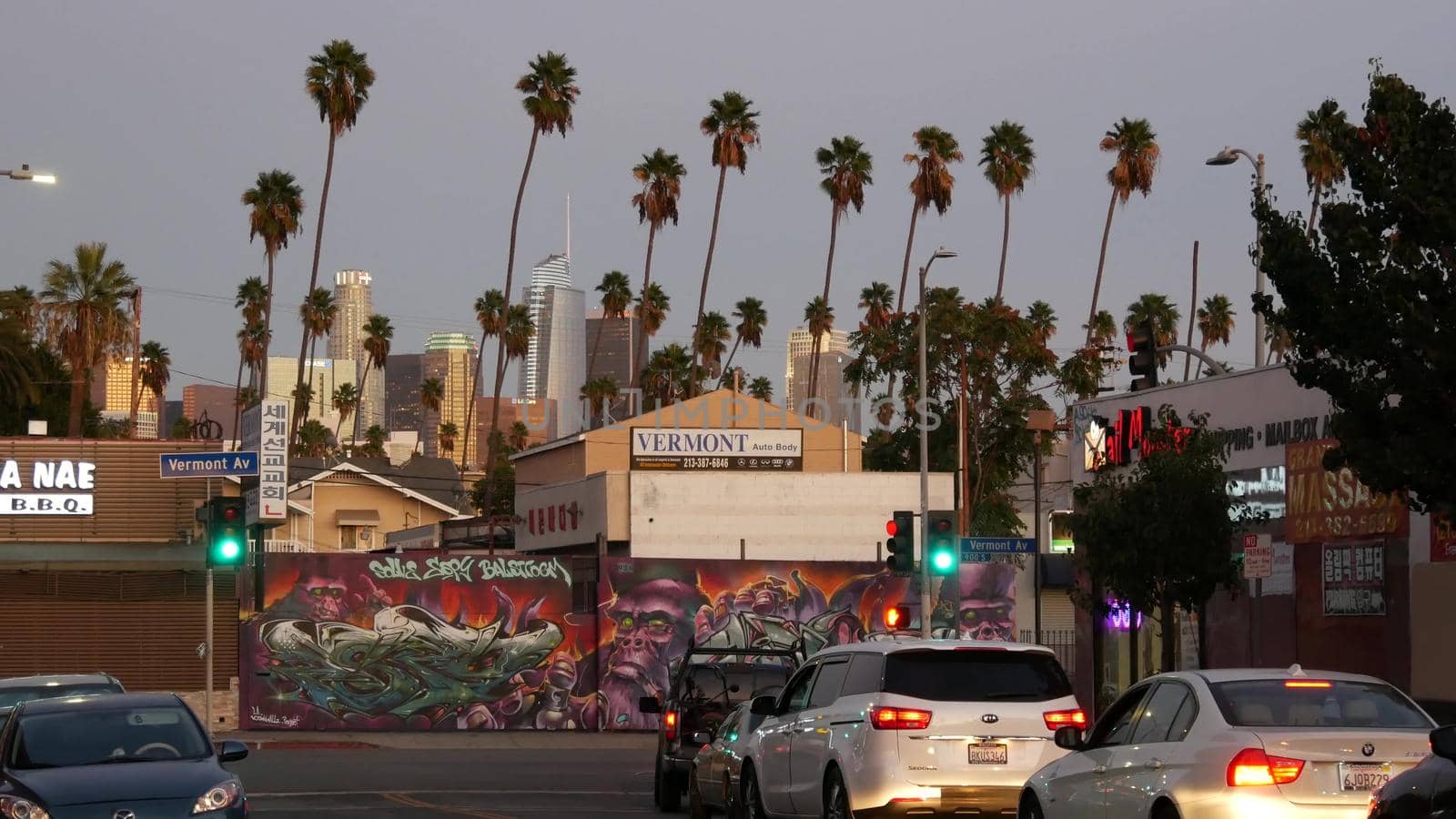 LOS ANGELES, CALIFORNIA, USA - 30 OCT 2019: Urban skyline and palms. LA city night aesthetic, graffiti painting on Vermont street. Highrise skyscrapers in downtown of metropolis. Road intersection.