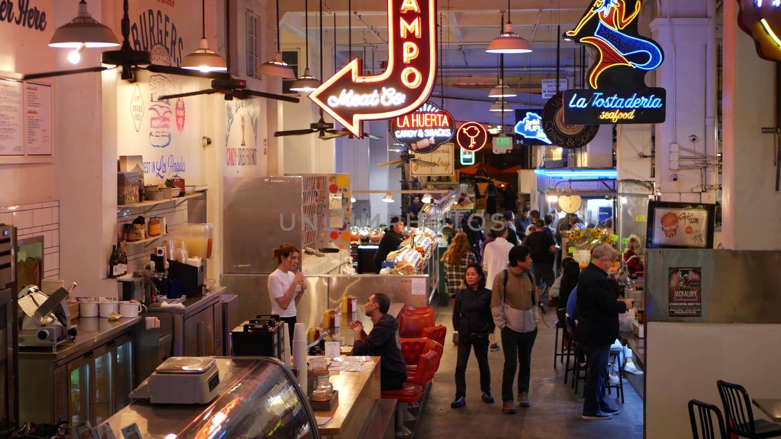 LOS ANGELES, CALIFORNIA, USA - 27 OCT 2019: Grand central market street lunch shops with diversity of glowing retro neon signs. Multiracial people on foodcourt. Citizens dining with fast food in LA.