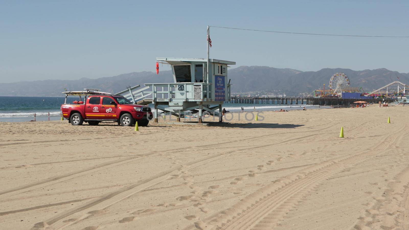SANTA MONICA, LOS ANGELES CA USA - 28 OCT 2019: California summertime beach aesthetic. Iconic blue wooden watchtower, red lifeguard car on sandy sunny coast. Amusement park and attractions on the pier