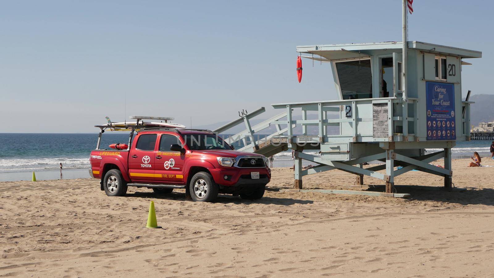 SANTA MONICA, LOS ANGELES CA USA - 28 OCT 2019: California summertime beach aesthetic. Iconic blue wooden watchtower, red lifeguard car on sandy sunny coast. Amusement park and attractions on the pier