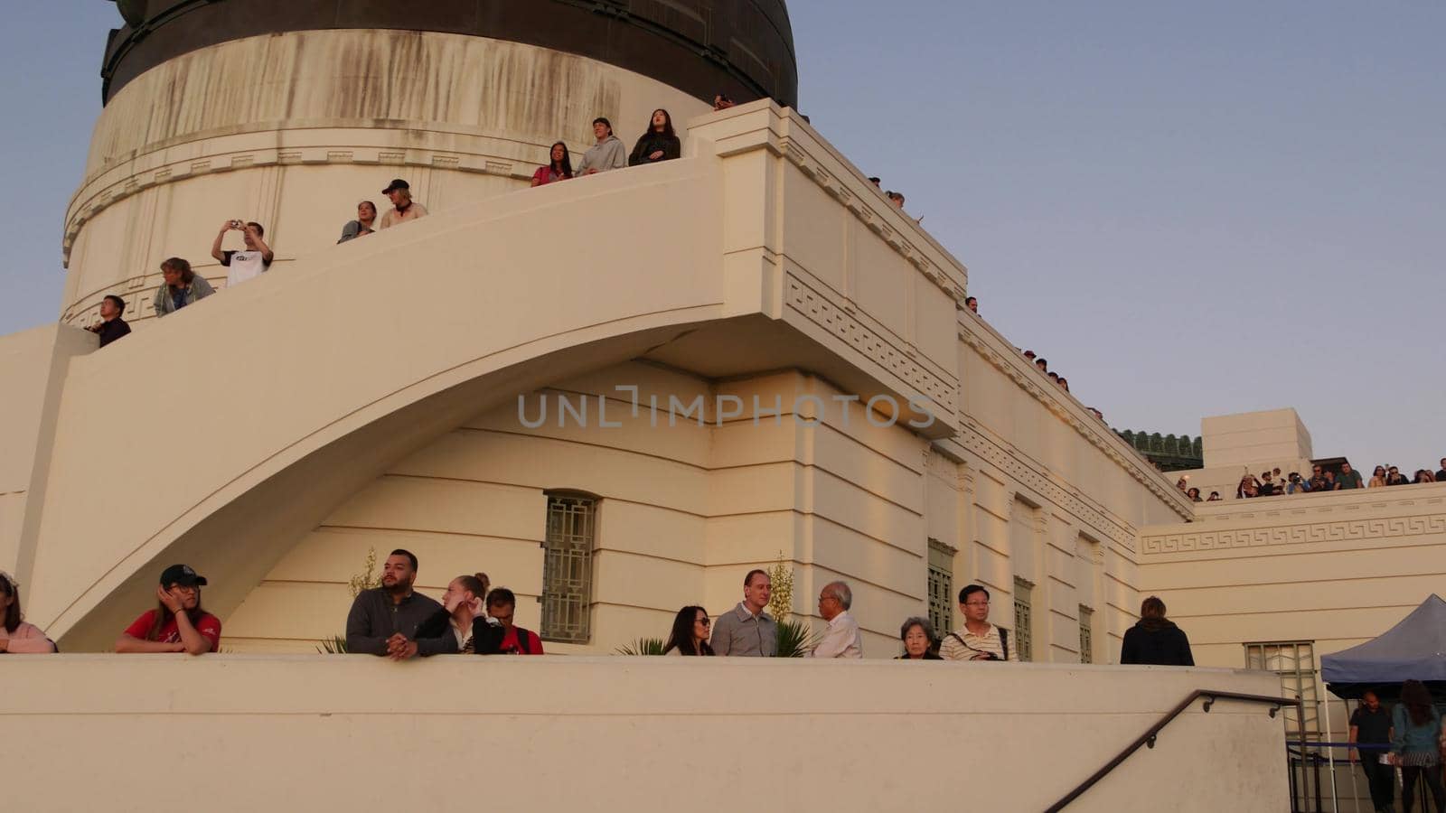 LOS ANGELES, CALIFORNIA, USA - 7 NOV 2019: Griffith observatory viewpoint. Crowd on vista point, people watching sunset over city and Hollywood sign. Many multiracial tourists look at golden sundown by DogoraSun