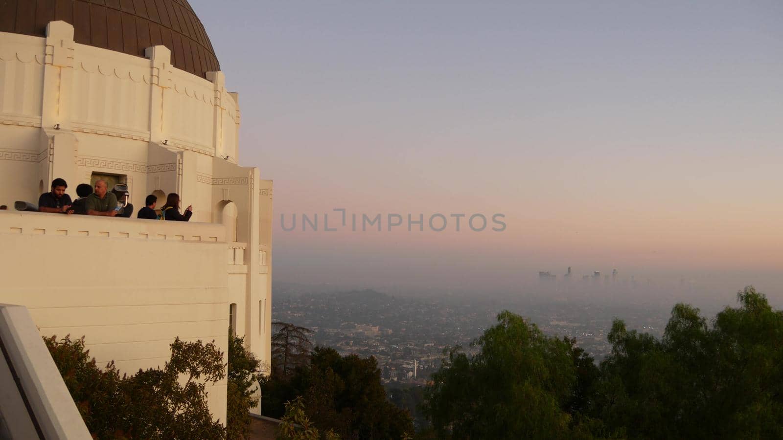 LOS ANGELES, CALIFORNIA, USA - 7 NOV 2019: Griffith observatory viewpoint. Crowd on vista point, people watching sunset over city and Hollywood sign. Many multiracial tourists look at golden sundown by DogoraSun