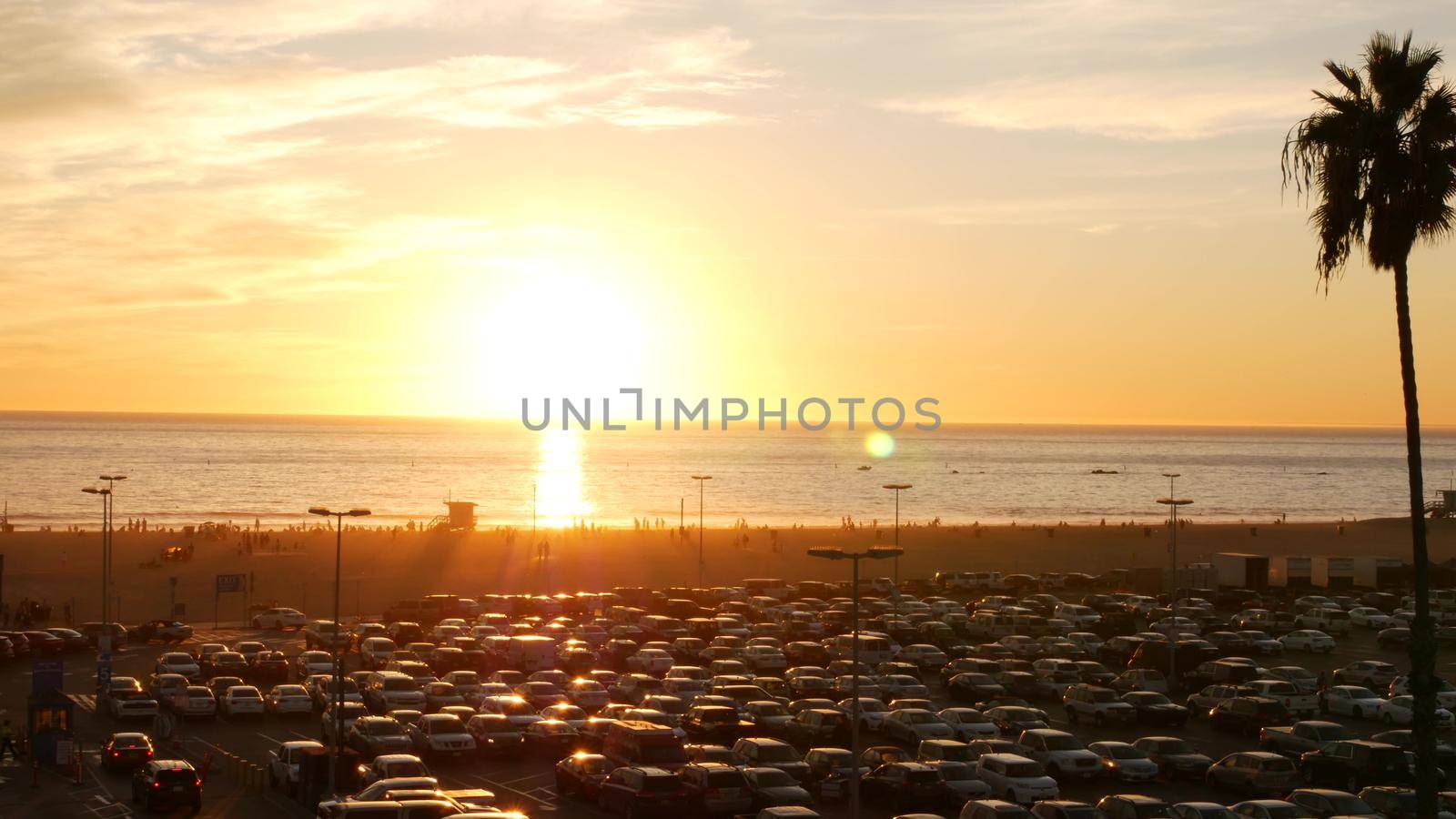 SANTA MONICA, LOS ANGELES, USA - 28 OCT 2019: California summertime beach aesthetic, atmospheric golden sunset. Unrecognizable people silhouettes, sun rays over pacific ocean waves. Lifeguard tower.