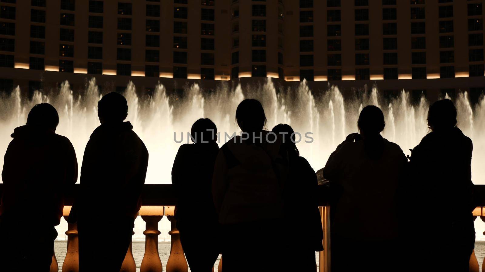 LAS VEGAS, NEVADA USA - 13 DEC 2019: People looking at Bellagio fountain musical performance at night. Contrast silhouettes and glowing dancing splashing water. Entertainment show in gambling city.