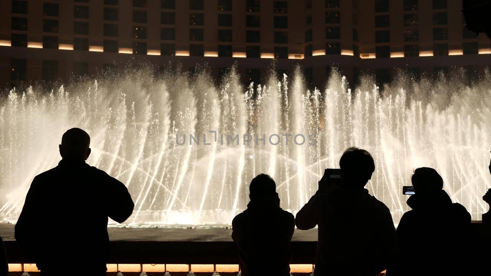 LAS VEGAS, NEVADA USA - 13 DEC 2019: People looking at Bellagio fountain musical performance at night. Contrast silhouettes and glowing dancing splashing water. Entertainment show in gambling city.