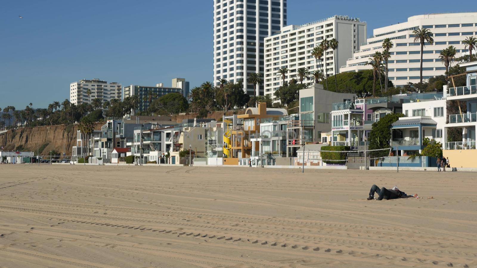 SANTA MONICA, LOS ANGELES CA USA - 19 DEC 2019: Alone anonymous man looks like unemployed and homeless sleeping on beach sand. Homelessness and begging crisis, social issue, poor people live on street