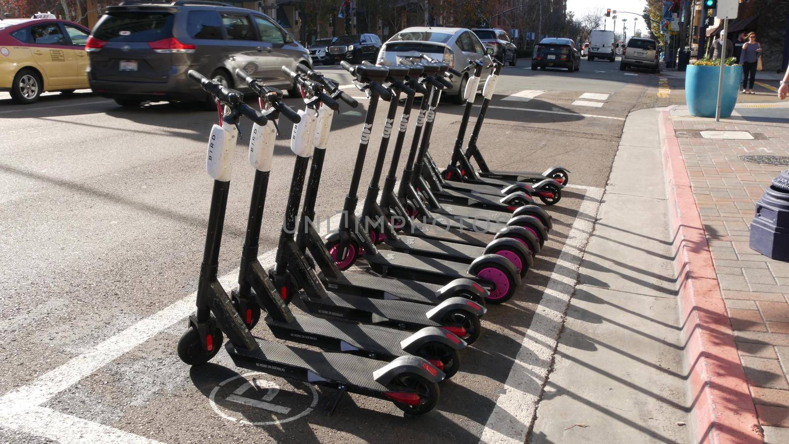 SAN DIEGO, CALIFORNIA USA - 4 JAN 2020: Row of ride sharing electric scooters parked on street in Gaslamp Quarter. Rental dockless public bikes, eco transport in city. Rent kick cycle with mobile app by DogoraSun