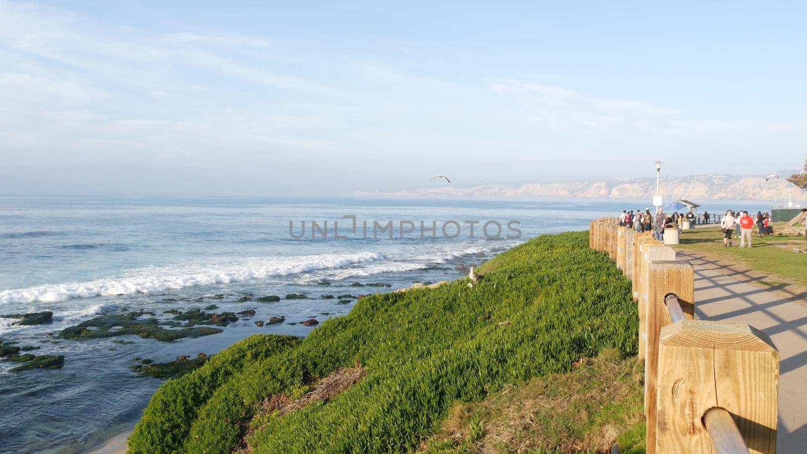 La Jolla, San Diego, CA USA -24 JAN 2020: Group of people walking on steep high cliff promenade, multiethnic pedestrians, tourists during holidays. Succulents and ocean, golden sunset in California.