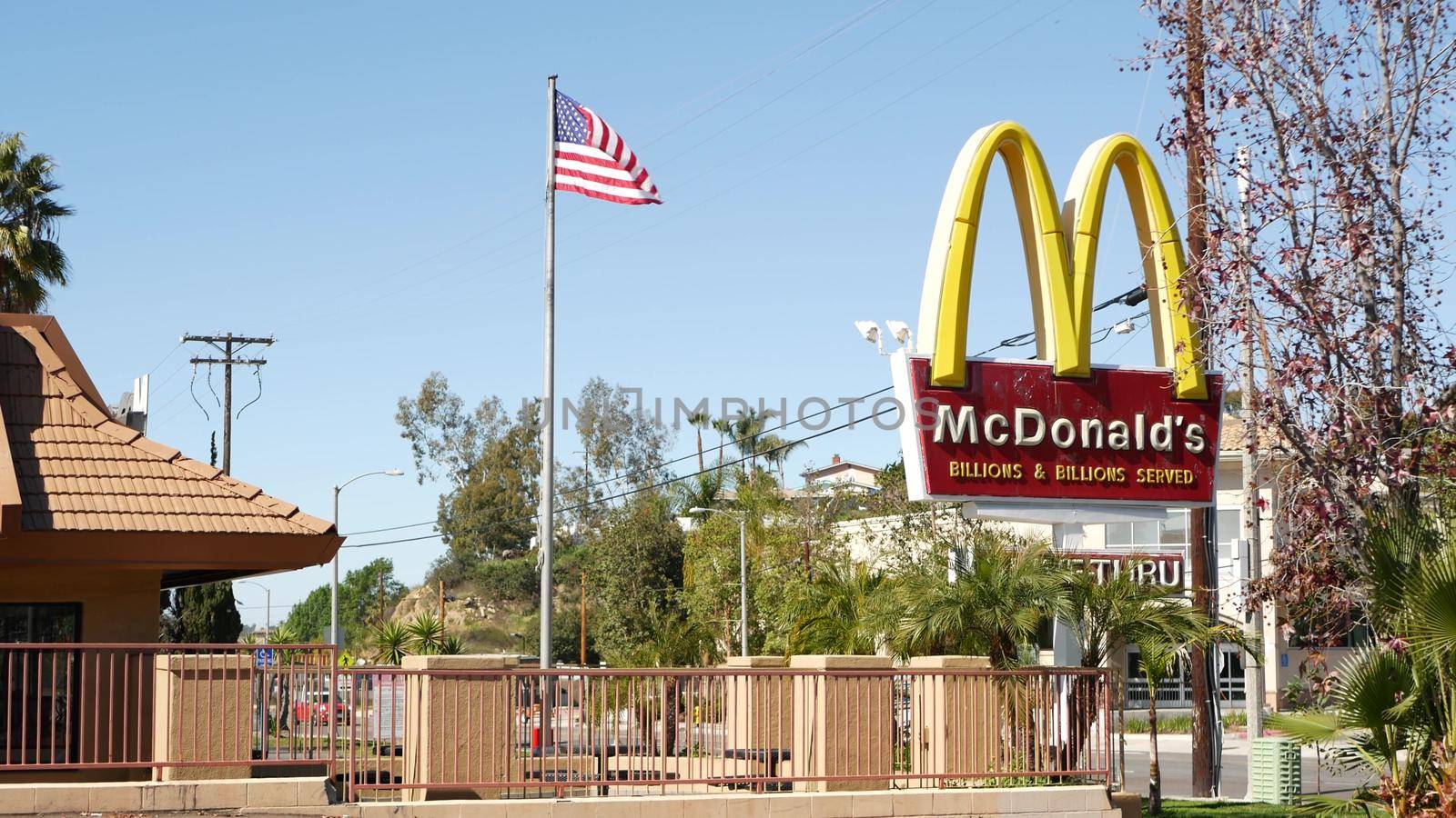 VISTA, CALIFORNIA USA - 16 FEB 2020 McDonalds logo sign and American flag. Yellow letter M icon and Stars and Stripes. Golden Arches emblem, brand sign in suburban district. Food restaurant on street by DogoraSun