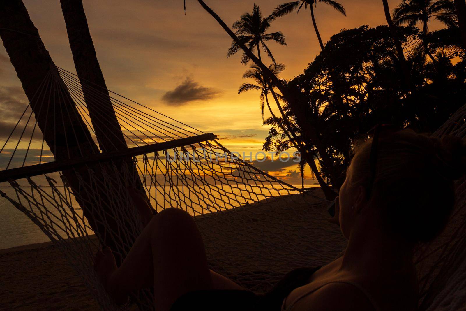 young women enyoing view of a colorful sunrise on the Tambua Sands Beach on Fiji Island in a hammock, Fiji by bettercallcurry