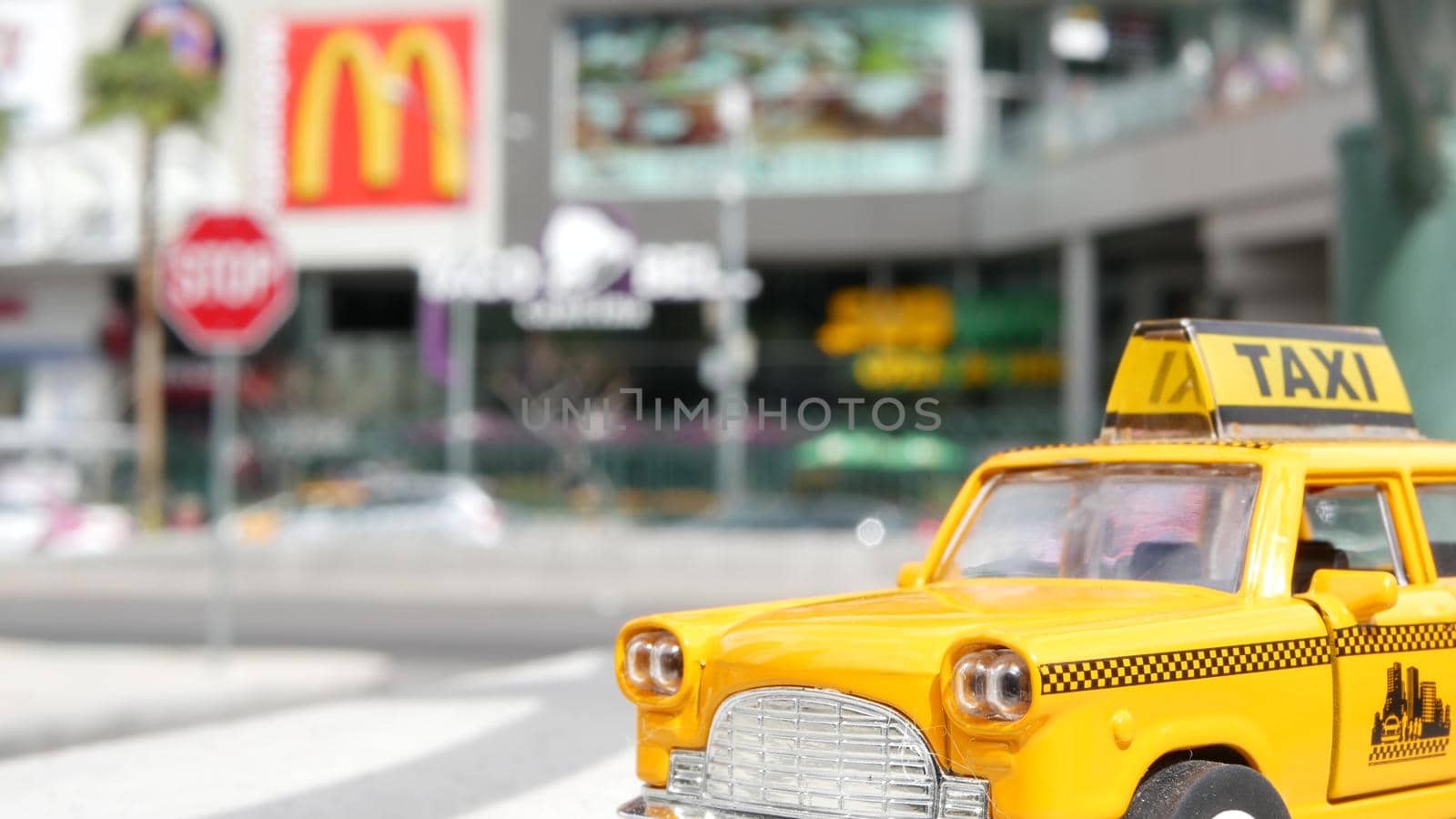 LAS VEGAS, NEVADA USA - 7 MAR 2020: Yellow vacant mini taxi cab close up on Harmon avenue corner. Small retro car model. Little iconic auto toy as symbol of transport against american shopping mall.