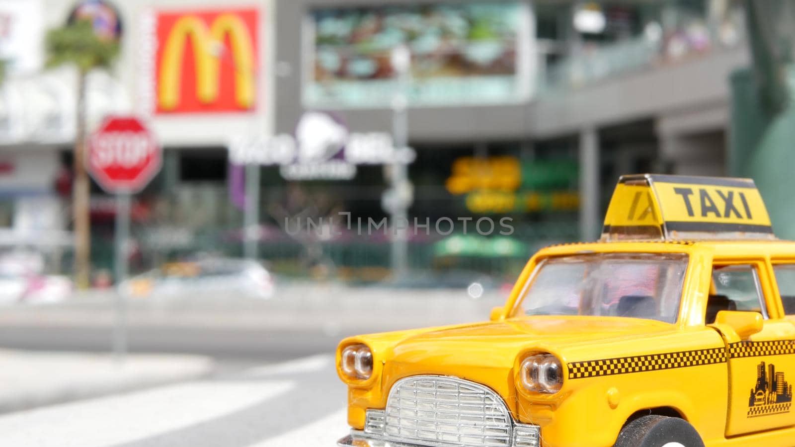 LAS VEGAS, NEVADA USA - 7 MAR 2020: Yellow vacant mini taxi cab close up on Harmon avenue corner. Small retro car model. Little iconic auto toy as symbol of transport against american shopping mall by DogoraSun