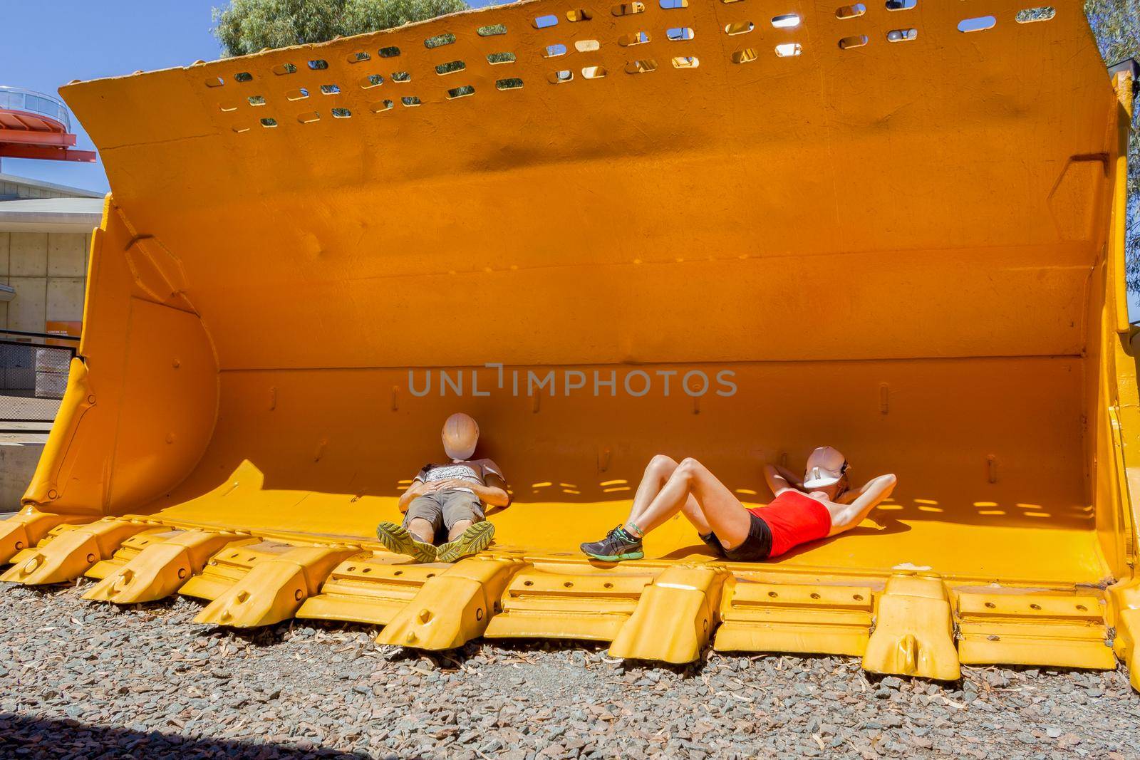 2 young people taking a nap in a mining front loader bucket for scale.