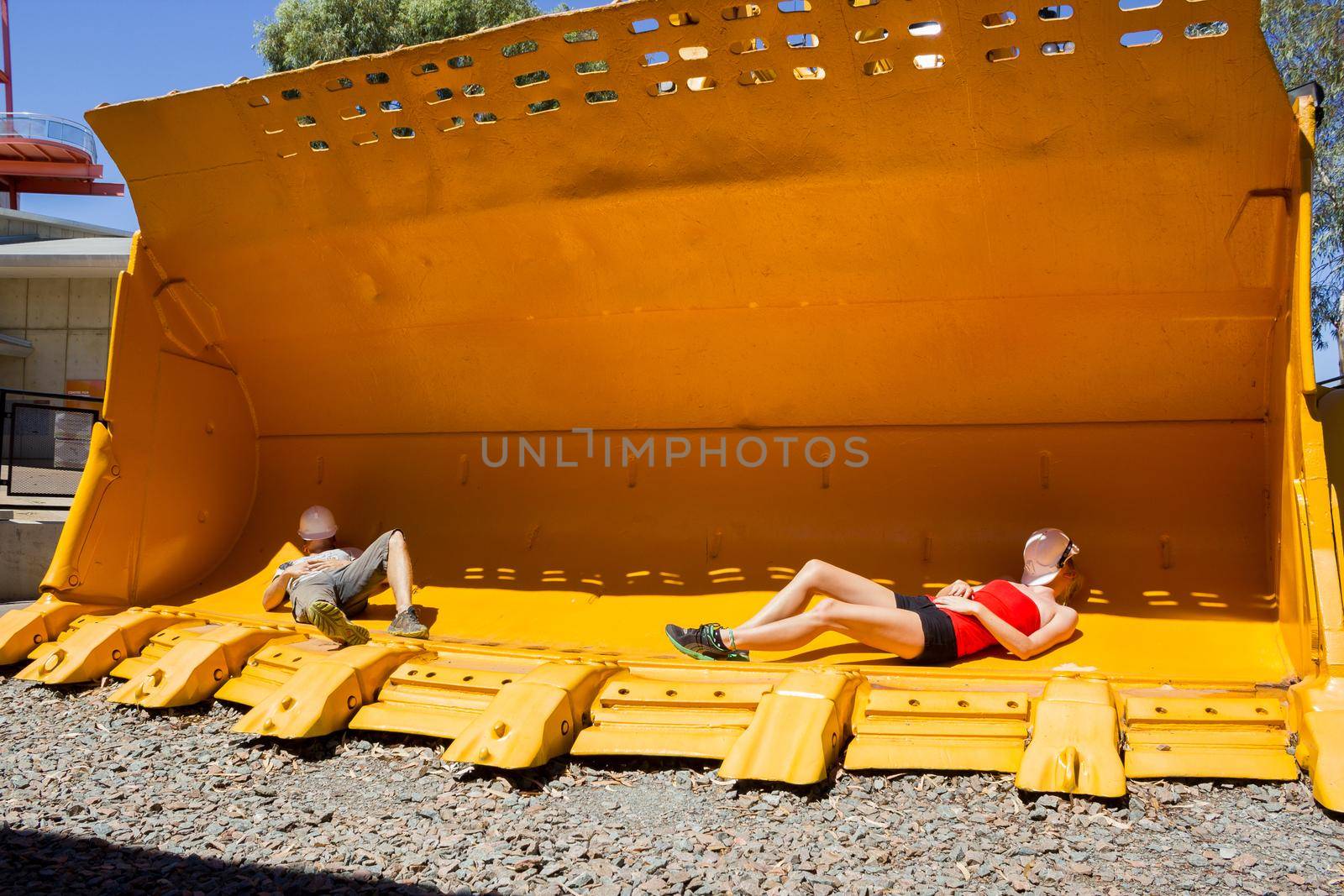 2 young people taking a nap in a mining front loader bucket for scale.