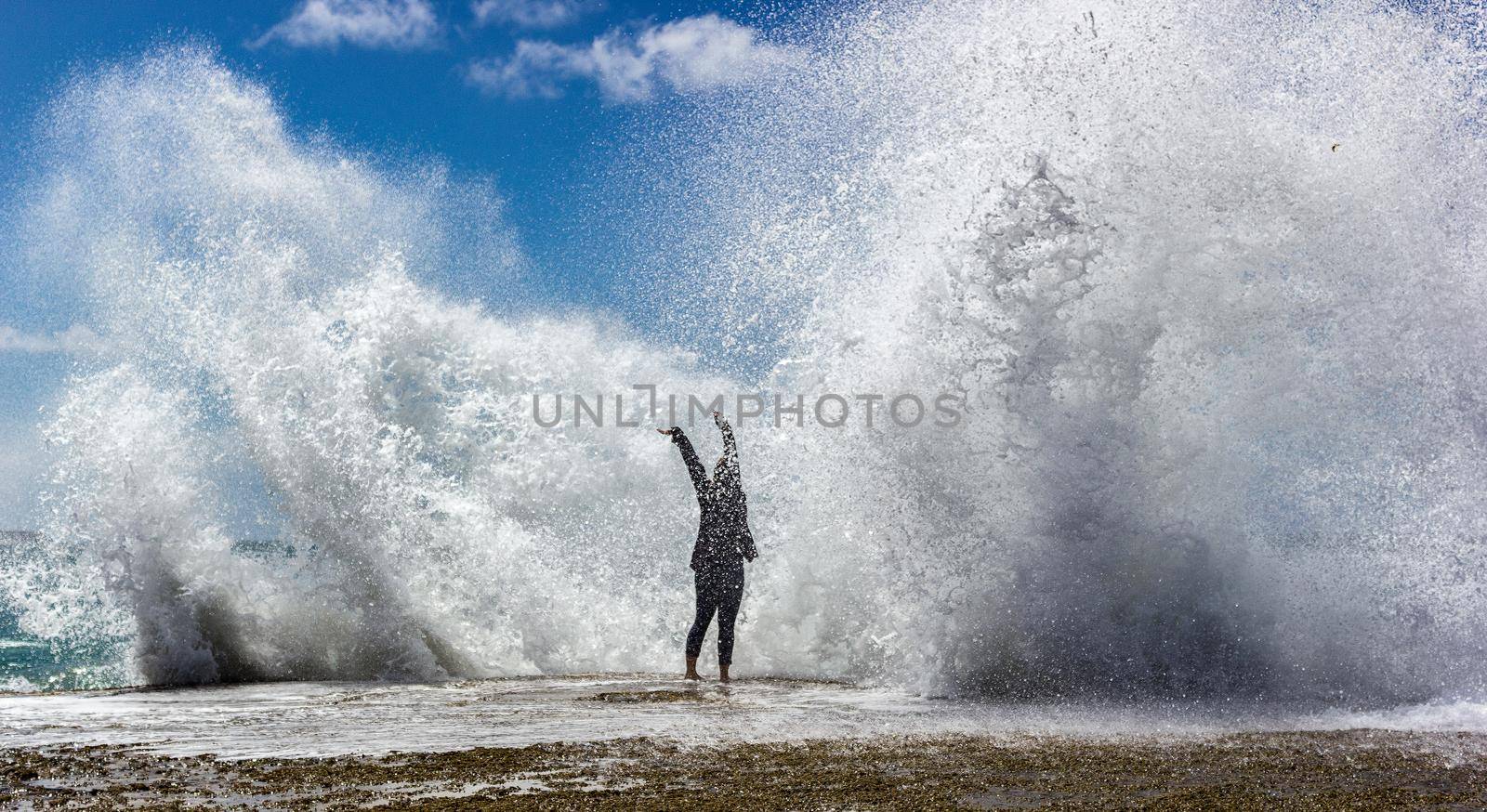 yung woman enjoying the moment when huge Powerful Waves crashing on rocks by bettercallcurry