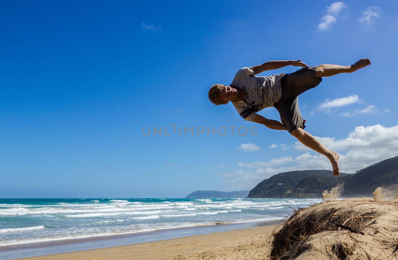 Portrait of young parkour man doing flip or somersault on the sand, Great Ocean Road, Australia by bettercallcurry