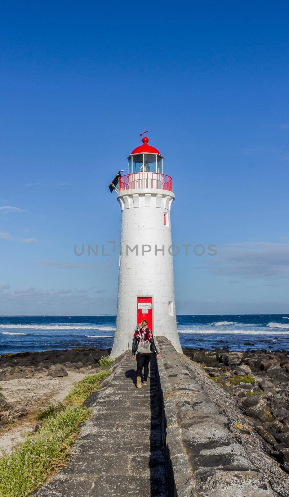 young woman dressed in black is walking towards a white lighthouse , Great Ocean Road by bettercallcurry