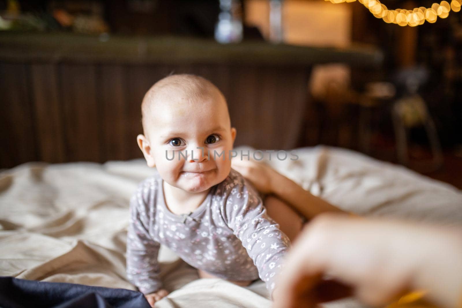 Adorable and happy baby lying on her stomach above bed with blurry background. Lovely baby on bed with cream color sheets. Cute toddlers