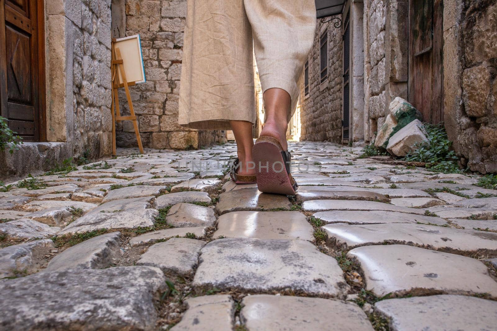 Detail shot of female legs wearing comfortable travel sandals walking on old medieval cobblestones street dring sightseeing city tour. Travel, tourism, and adventure concept.