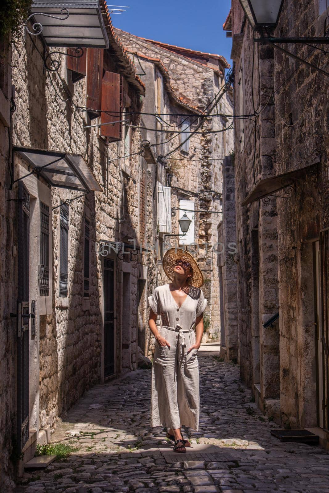 Beautiful blonde young female traveler wearing straw sun hat sightseeing and enjoying summer vacation in an old traditional costal town at Adriatic cost, Croatia.