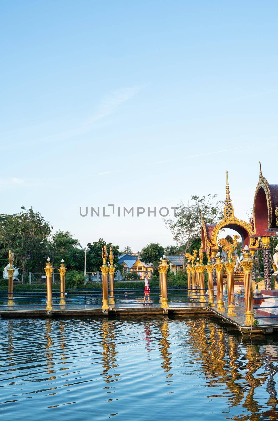 KOH SAMUI, THAILAND - January 10, 2020: Woman in a red dress standing on a bridge to a giant colorful buddha statue at wat plai laem temple on koh samui thailand