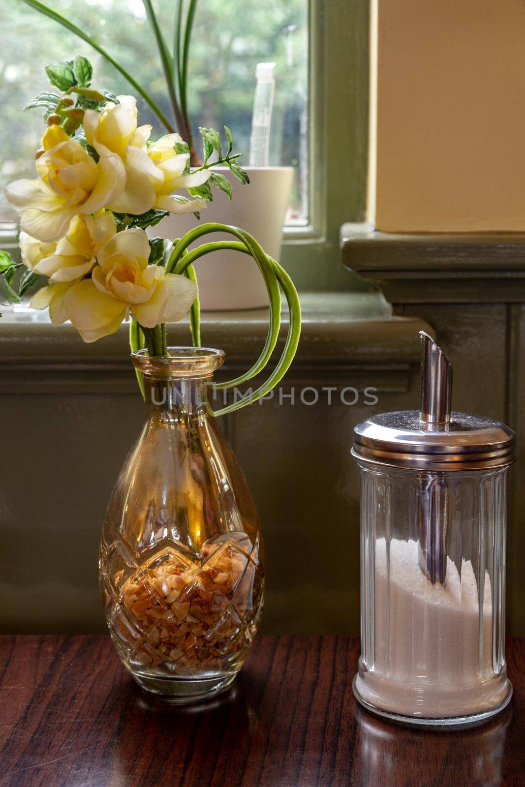 Yellow flowers in a glass vase on cafe table by a sugar jar