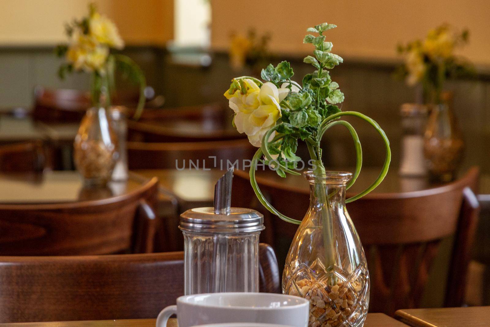 Yellow flowers in a glass vase on cafe table by a sugar jar