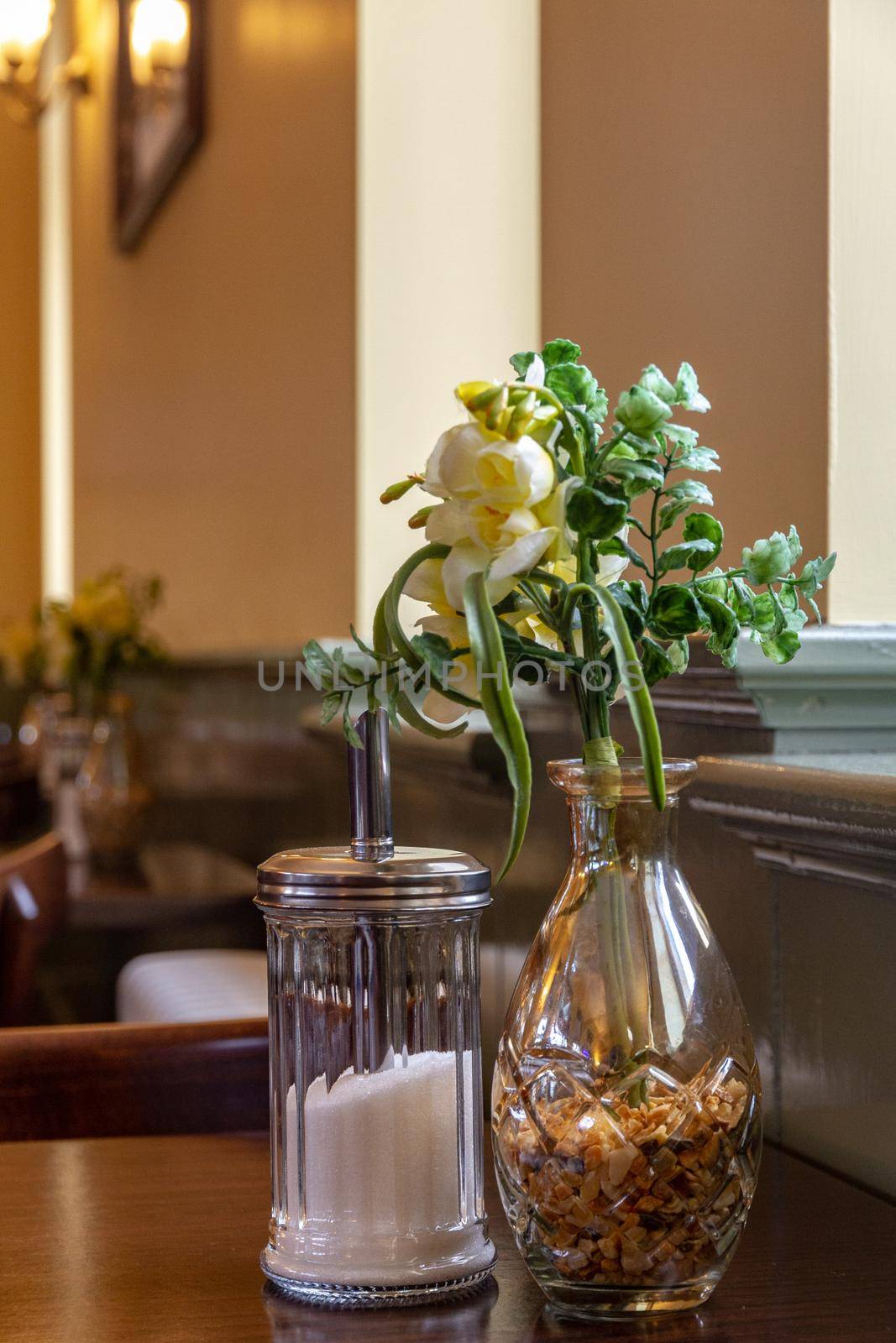 Yellow flowers in a glass vase on cafe table by a sugar jar