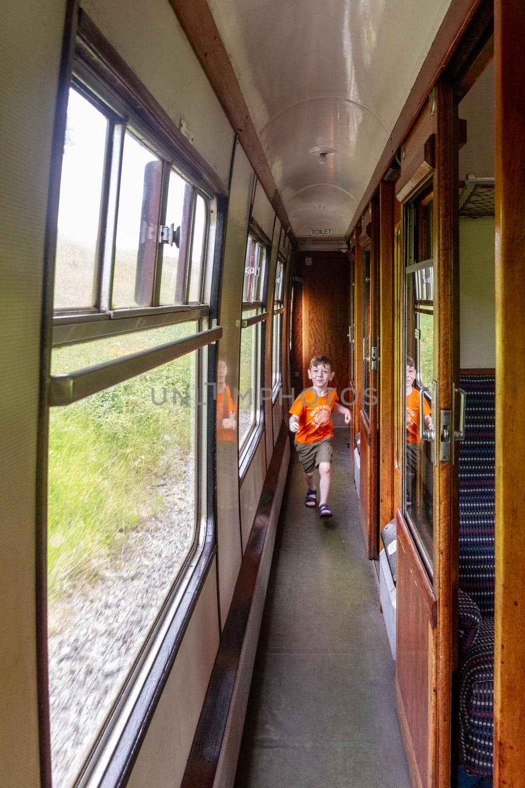 A cute, red-haired, blue-eyed four years old boy running through an old passenger train carriage