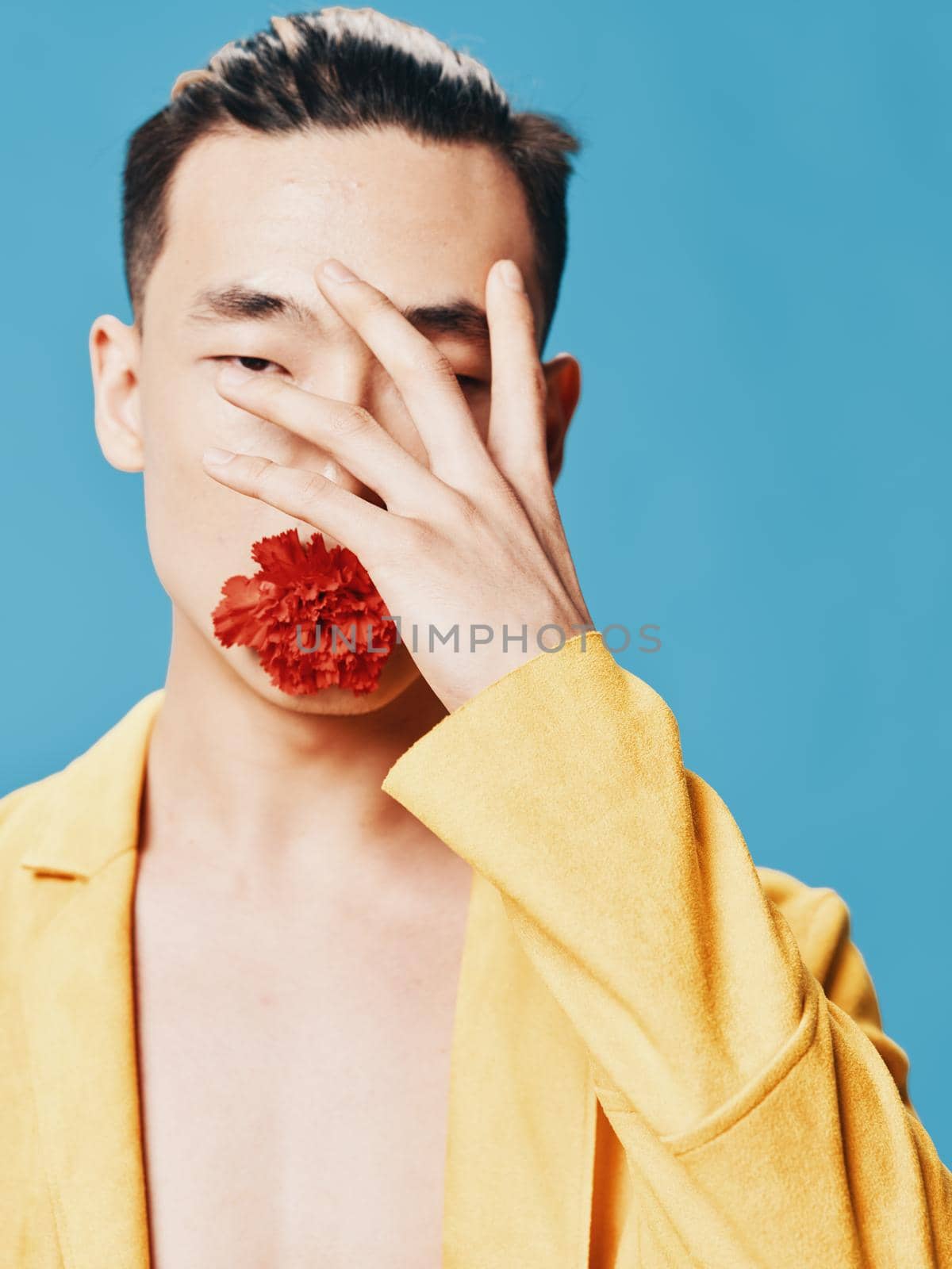 A man touches his face with his hand and a red flower in his mouth on a blue background. High quality photo