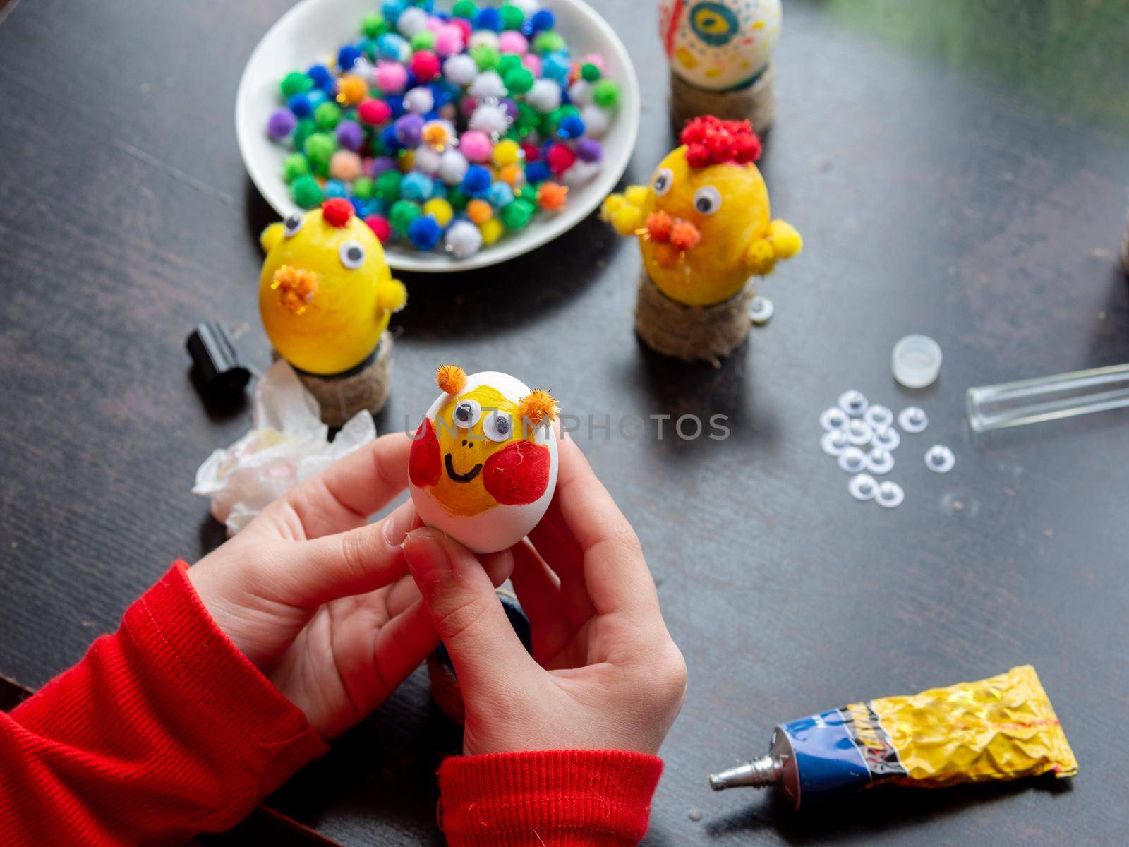 The girl is holding a beautifully painted egg with a smiling painted face