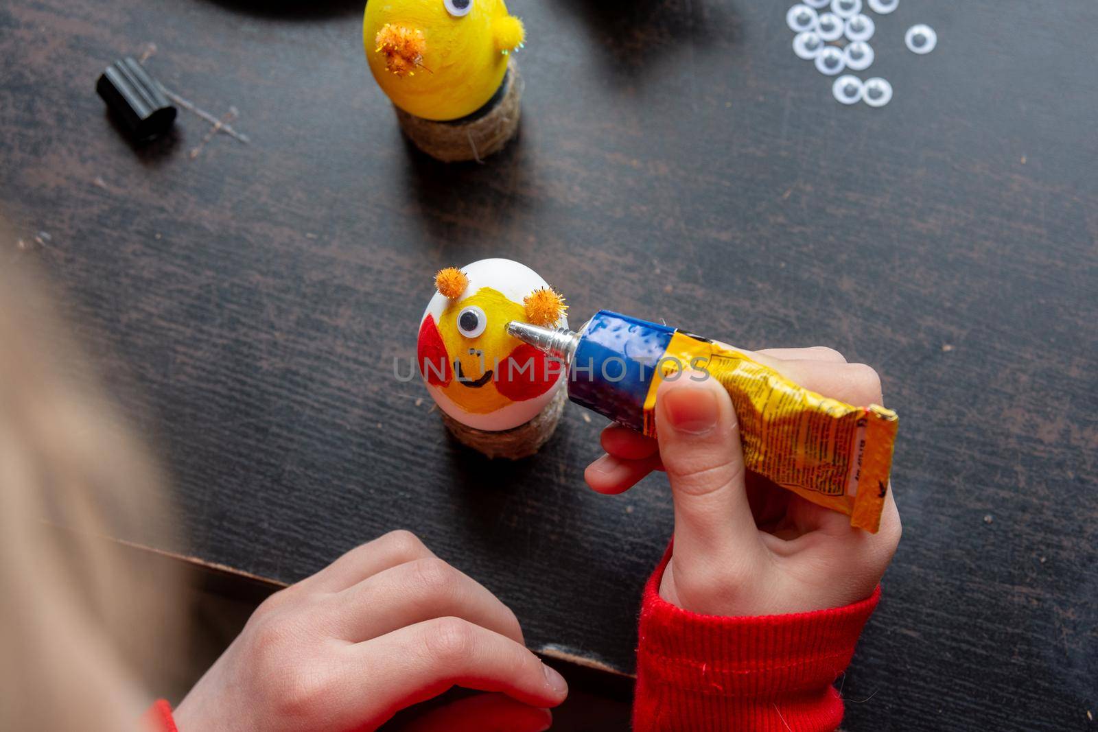 A girl decorates an egg for easter and glues funny eyes to it