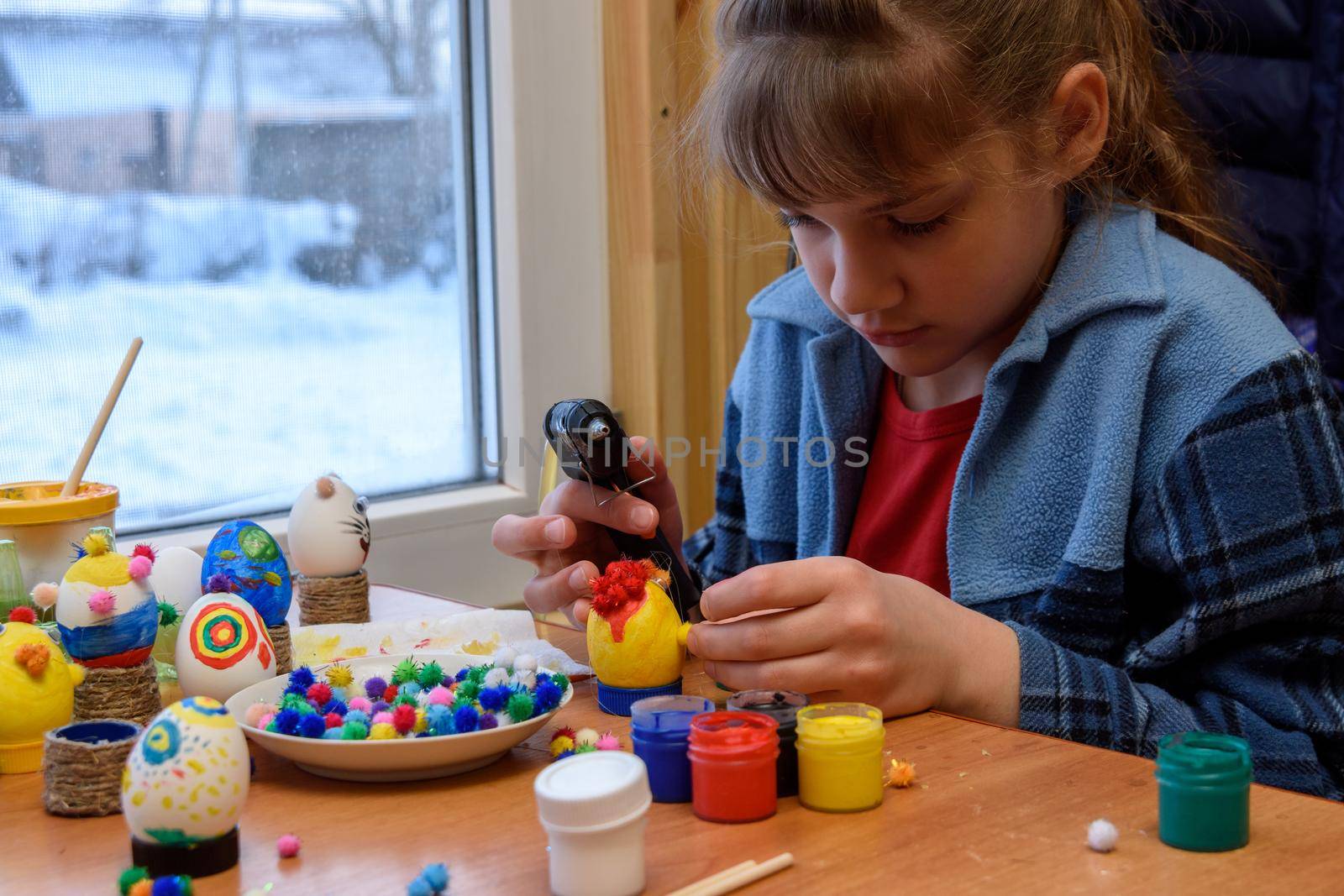 A girl glues a decorative element to a craft with a glue gun