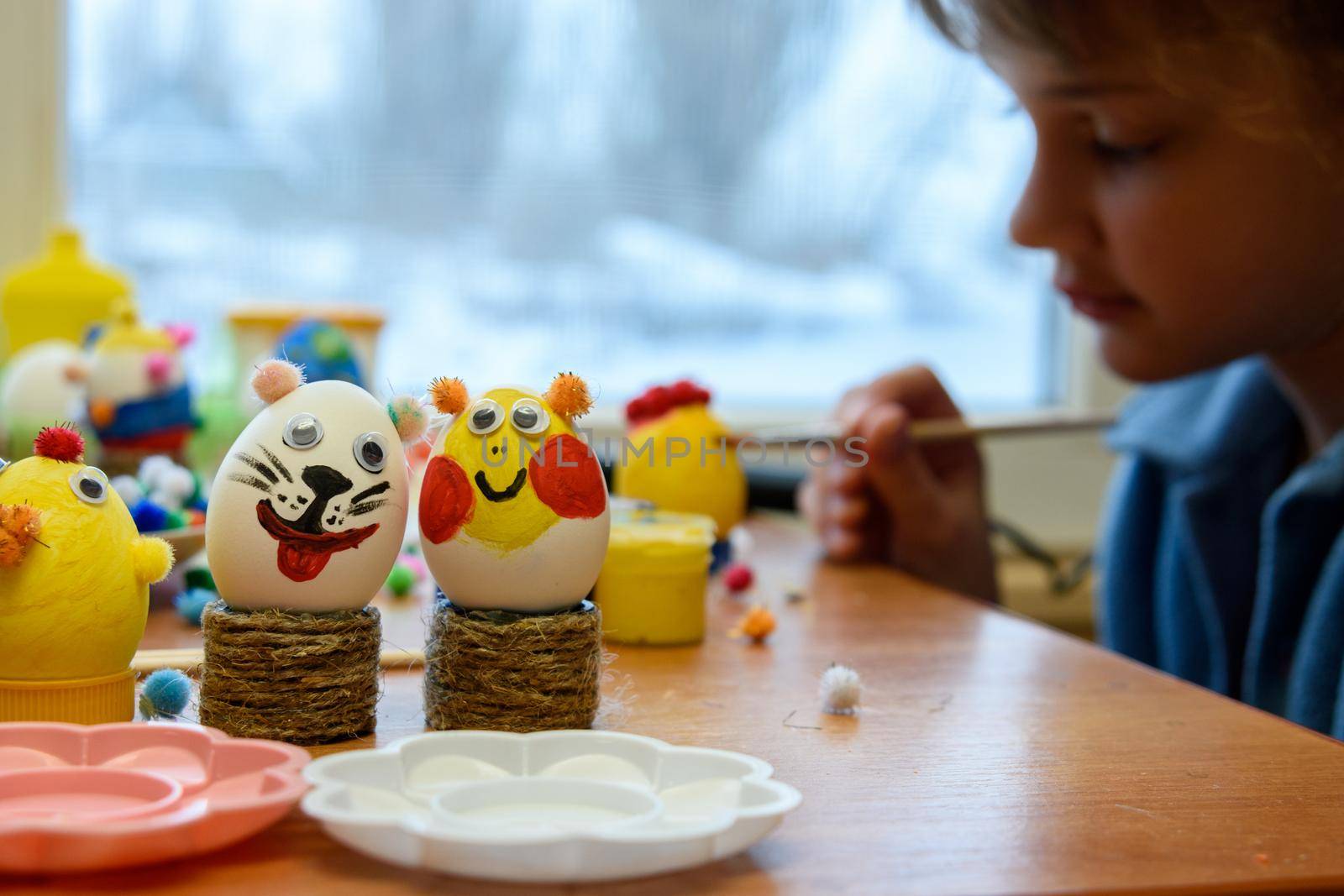 In the foreground there are decorated children's Easter eggs, in the background a child is painting an egg