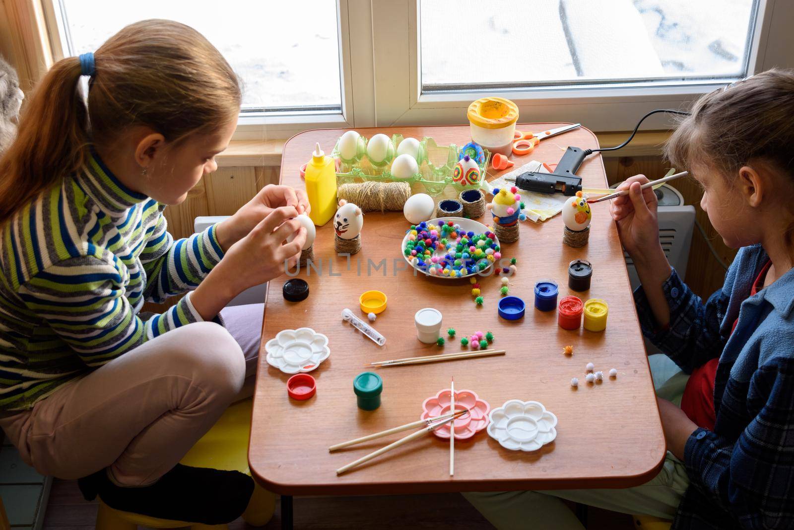 Two girls at the table are painting Easter eggs