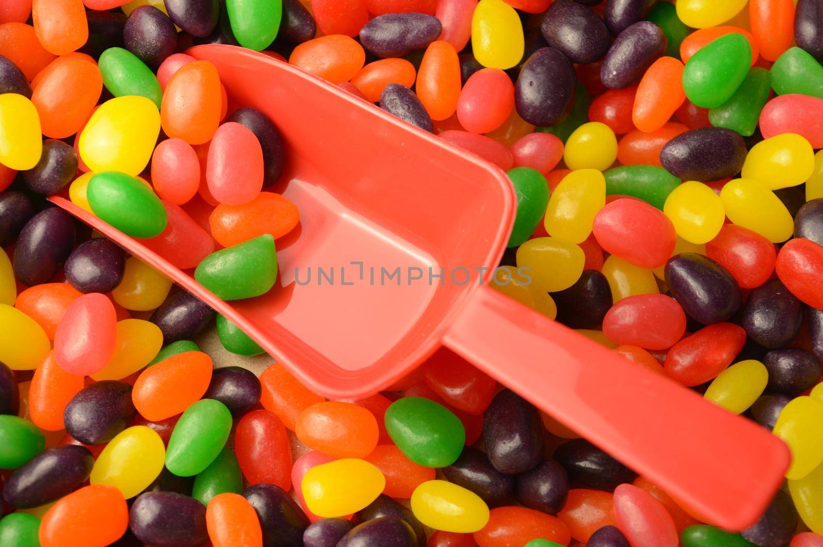A closeup view of a red scoop in an abundant supply of jelly bean candy.