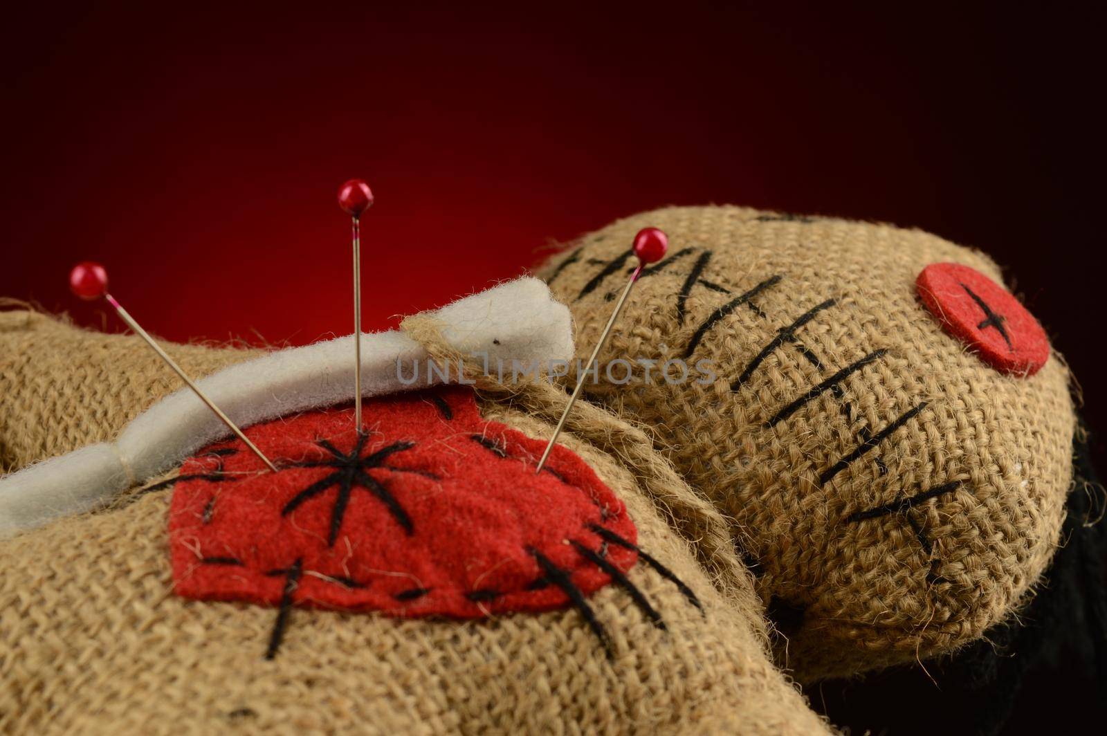 A few pins are stuck inside the heart of a voodoo doll over a dark red and black background.