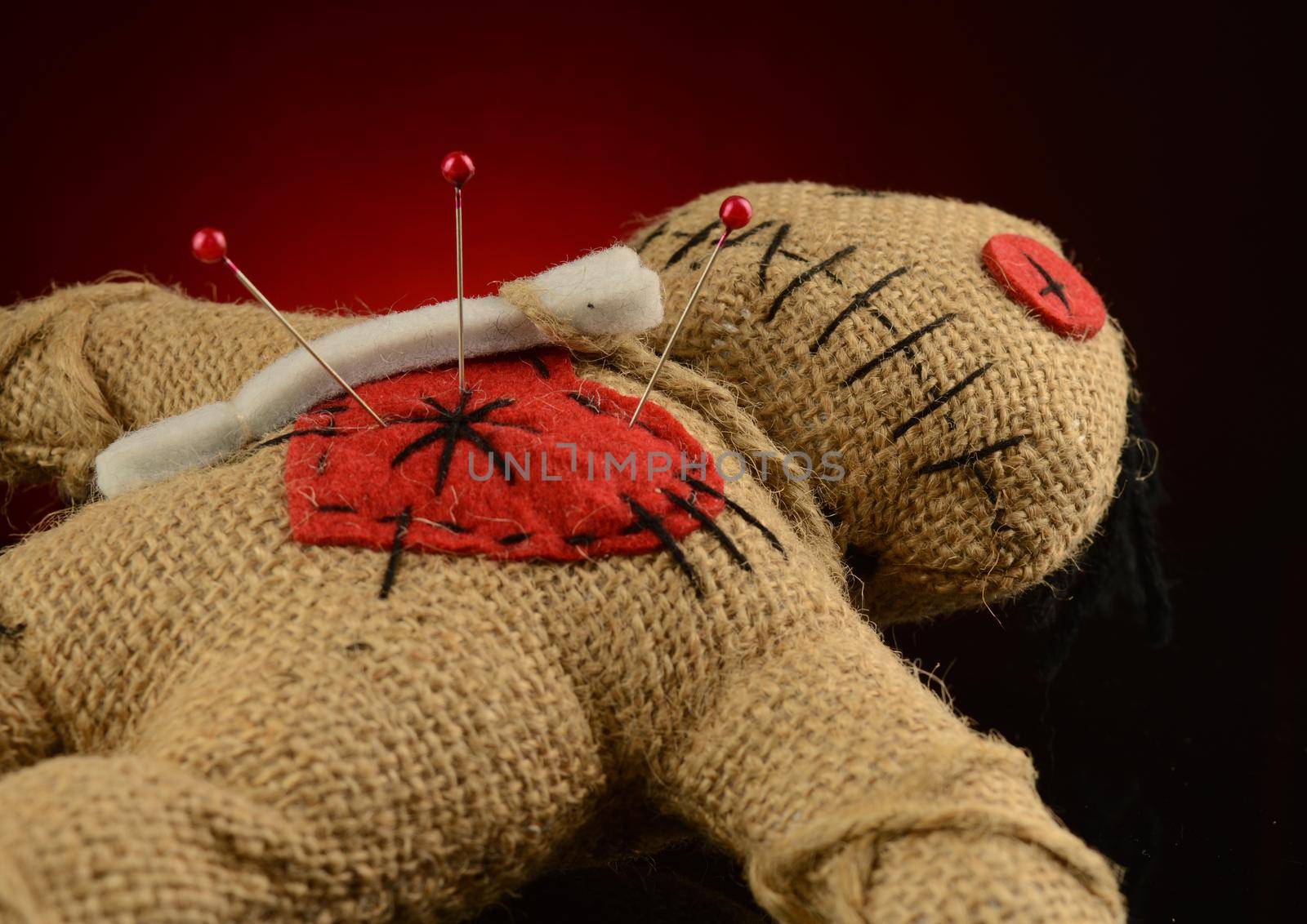 A few pins are stuck inside the heart of a voodoo doll over a dark red and black background.