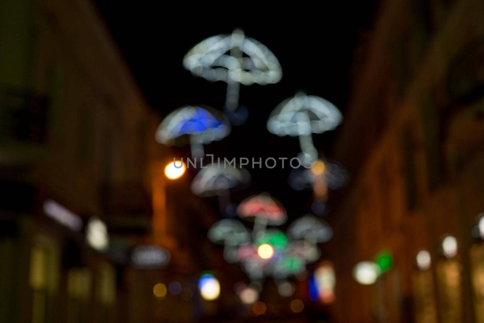 Blurred background of the city at night with bright glowing silhouettes of umbrellas