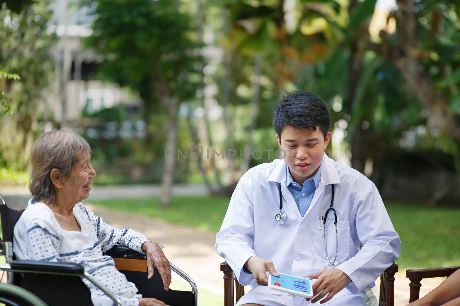 Asian doctor talking with elderly female patient on wheelchair