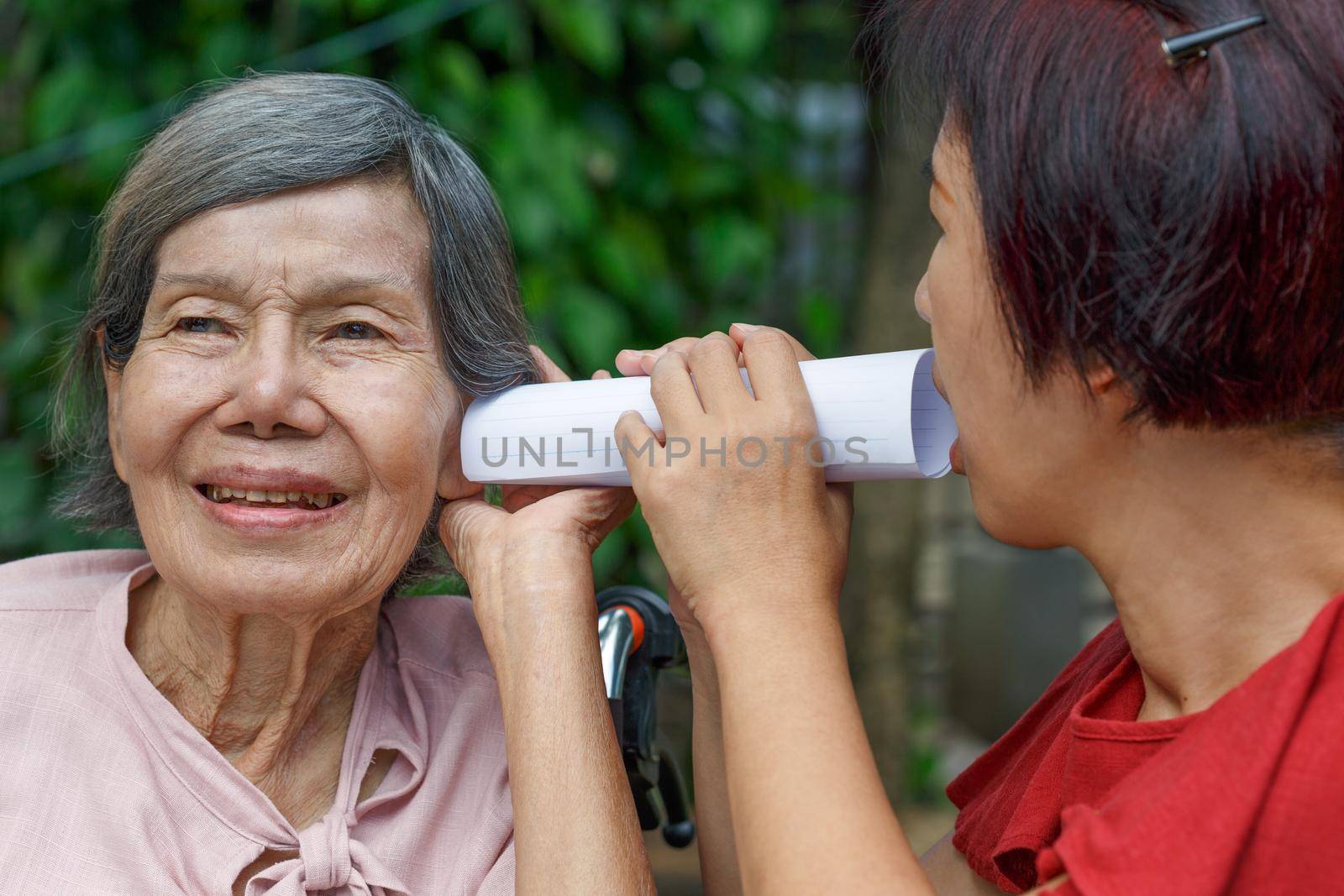 Daughter talking to hearing impaired elderly woman , using paper tube