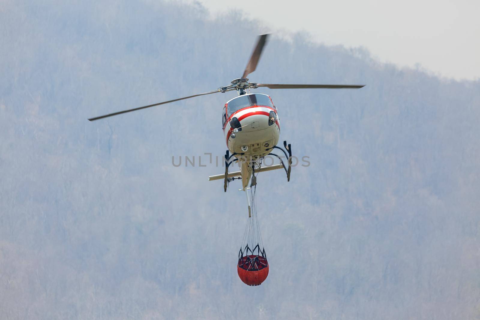 Firefighting  helicopter carrying  water bucket for 
extinguish forest fire ,  comeback at lake to filling water by toa55