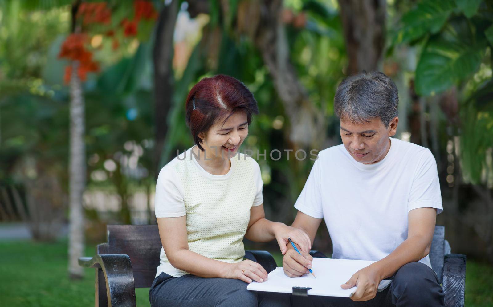 Asian middle-aged couple talking and designing garden plan together in backyard.