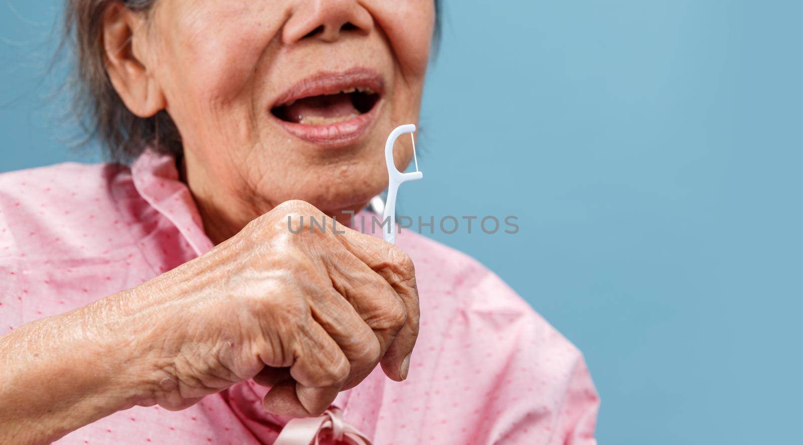 Caregiver take care asian elderly woman while using dental fross stick.