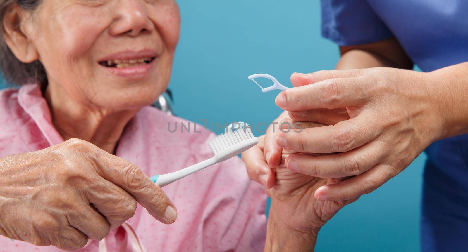 Caregiver take care asian elderly woman while using dental fross stick.