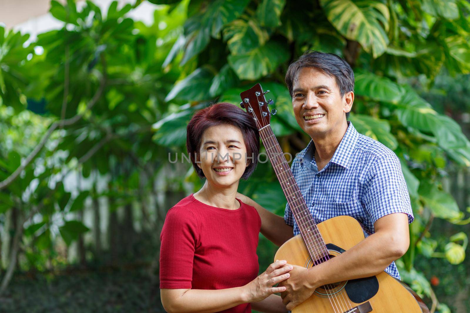 Middle aged  couple playing guitar while relax sitting on bench in backyard. by toa55