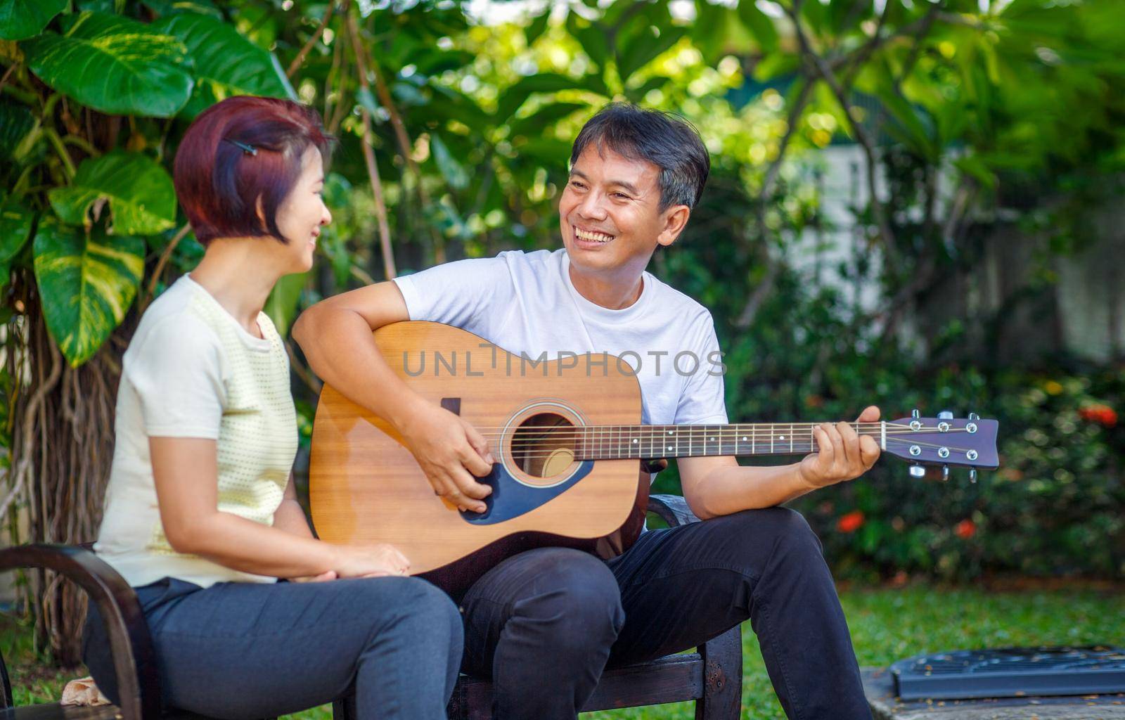 Middle aged  couple playing guitar while relax sitting on bench in backyard. by toa55