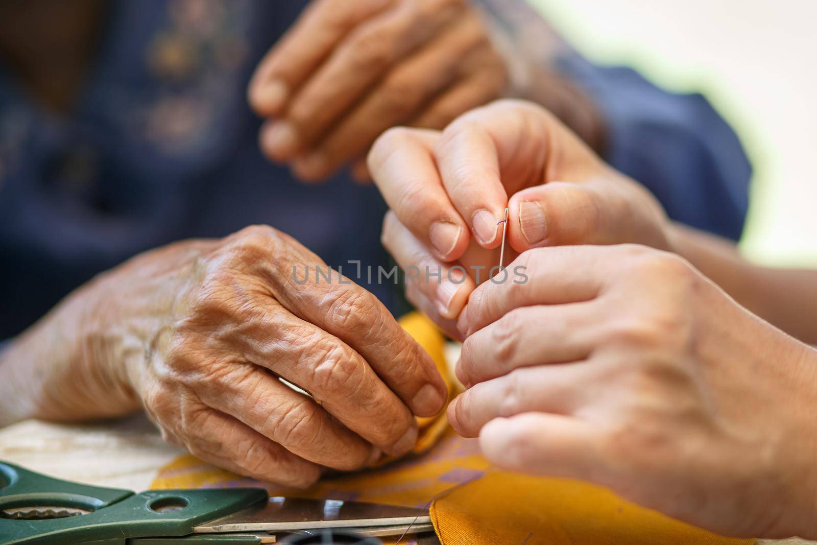 Caregiver holding thread the needle for elderly woman in the cloth crafts occupational therapy for Alzheimers or dementia